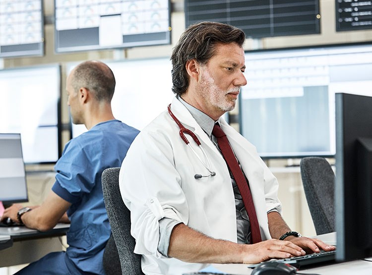 A doctor entering data on a keyboard and desktop in the hospital.